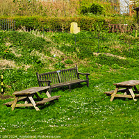 Buy canvas prints of Rustic wooden benches and a table on a lush green grassy hillside, with a stone building and vegetation in the background, depicting a serene outdoor setting in York, North Yorkshire, England. by Man And Life