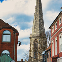 Buy canvas prints of Vertical shot of an ancient church spire reaching into a blue sky with clouds, flanked by traditional brick buildings, showcasing architectural contrast and historical cityscape in York, North Yorkshire, England. by Man And Life