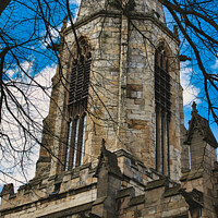 Buy canvas prints of Gothic church tower with intricate stone details, framed by bare tree branches against a blue sky with fluffy clouds in York, North Yorkshire, England. by Man And Life