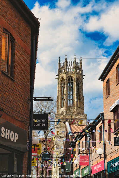 Quaint urban street with festive bunting leading to a historic church tower under a blue sky with fluffy clouds in York, North Yorkshire, England. Picture Board by Man And Life