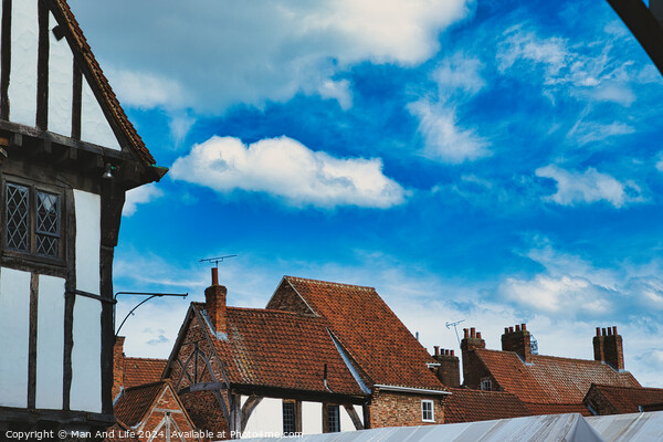 Quaint European village with traditional half-timbered houses and terracotta rooftops under a vibrant blue sky with fluffy clouds in York, North Yorkshire, England. Picture Board by Man And Life