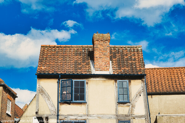 Old European building with weathered facade and terracotta roof tiles against a backdrop of a vibrant blue sky with fluffy clouds in York, North Yorkshire, England. Picture Board by Man And Life