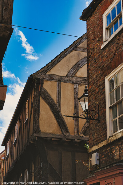 Quaint half-timbered building with exposed wooden beams under a clear blue sky, showcasing traditional architectural details and a vintage street lamp in York, North Yorkshire, England. Picture Board by Man And Life