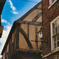 Buy canvas prints of Quaint half-timbered building with exposed wooden beams under a clear blue sky, showcasing traditional architectural details and a vintage street lamp in York, North Yorkshire, England. by Man And Life