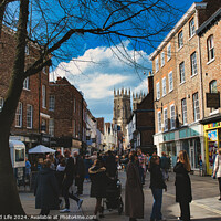 Buy canvas prints of Bustling city street scene with pedestrians, historic buildings, and a cathedral spire under a blue sky with scattered clouds in York, North Yorkshire, England. by Man And Life