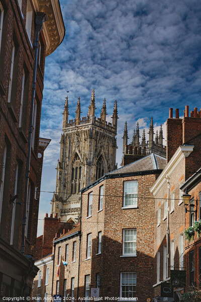 Quaint cobbled street leading to a majestic Gothic cathedral under a blue sky with wispy clouds, showcasing historical architecture and urban charm in York, North Yorkshire, England. Picture Board by Man And Life
