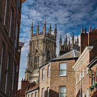 Buy canvas prints of Quaint cobbled street leading to a majestic Gothic cathedral under a blue sky with wispy clouds, showcasing historical architecture and urban charm in York, North Yorkshire, England. by Man And Life