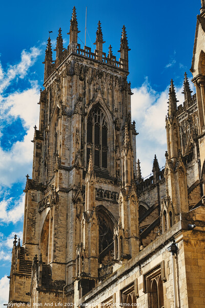 Gothic cathedral tower against a blue sky with clouds, showcasing intricate architectural details and flying buttresses in York, North Yorkshire, England. Picture Board by Man And Life