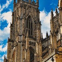 Buy canvas prints of Gothic cathedral tower against a blue sky with clouds, showcasing intricate architectural details and flying buttresses in York, North Yorkshire, England. by Man And Life