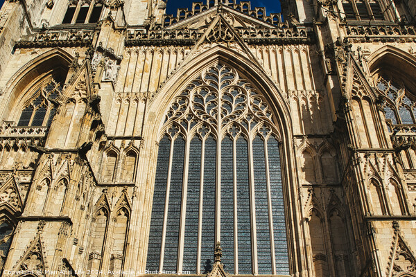 Gothic architecture detail of a cathedral's facade, featuring a large stained glass window and ornate stone carvings under clear skies in York, North Yorkshire, England. Picture Board by Man And Life