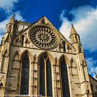 Buy canvas prints of Gothic cathedral facade with rose window and spires against a blue sky with clouds, framed by trees in York, North Yorkshire, England. by Man And Life