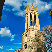 Buy canvas prints of Gothic church tower against a vibrant blue sky with fluffy clouds, showcasing intricate architectural details and a blooming tree at the corner in York, North Yorkshire, England. by Man And Life