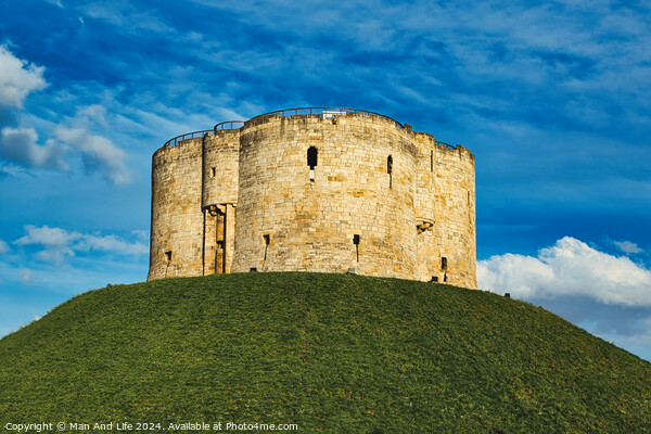 Medieval stone tower atop a lush green hill against a vibrant blue sky with fluffy clouds, symbolizing historical fortification and ancient architecture in York, North Yorkshire, England. Picture Board by Man And Life