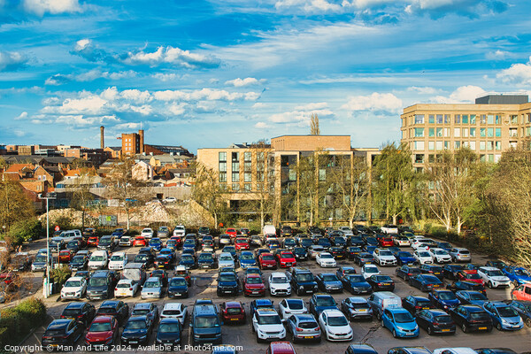 Urban parking lot filled with cars on a sunny day, with city buildings in the background and a clear blue sky overhead in York, North Yorkshire, England. Picture Board by Man And Life