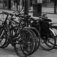 Buy canvas prints of Black and white image of multiple bicycles locked to a bike rack in an urban setting, with a blurred background of a city street by Man And Life