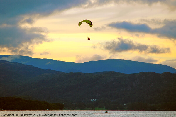 Paraglider flies above Windermere at dusk. Picture Board by Phil Brown