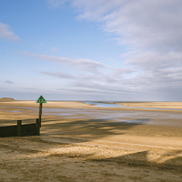 Buy canvas prints of Green groyne marker and sunlit beach under a heavy by Liam Grant