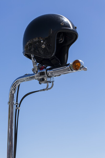 Open face crash helmet on handlebars of a motorcycle against a blue sky Picture Board by Phil Crean
