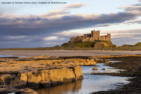 Bamburgh Castle from Harkness Rocks sunset Picture Board by Graham Moore