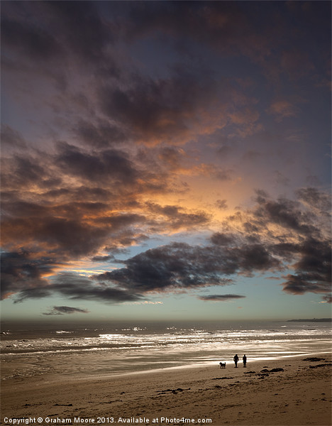 Couple walking on beach at sunset Picture Board by Graham Moore